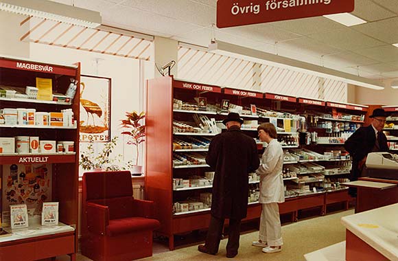 Interiör från apoteket Tranan i Vänersborg 1981. Självvalsavdelningen i apoteket Tranan. En kund får information.