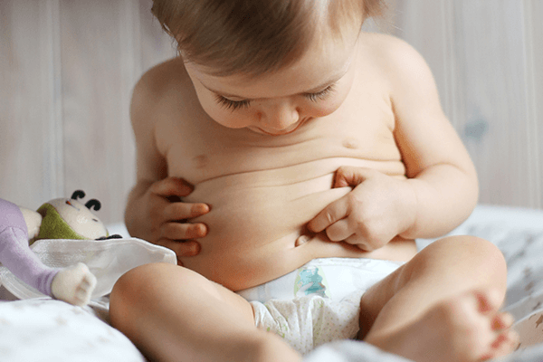 Bebis med förstoppad mage petar med finger på mage