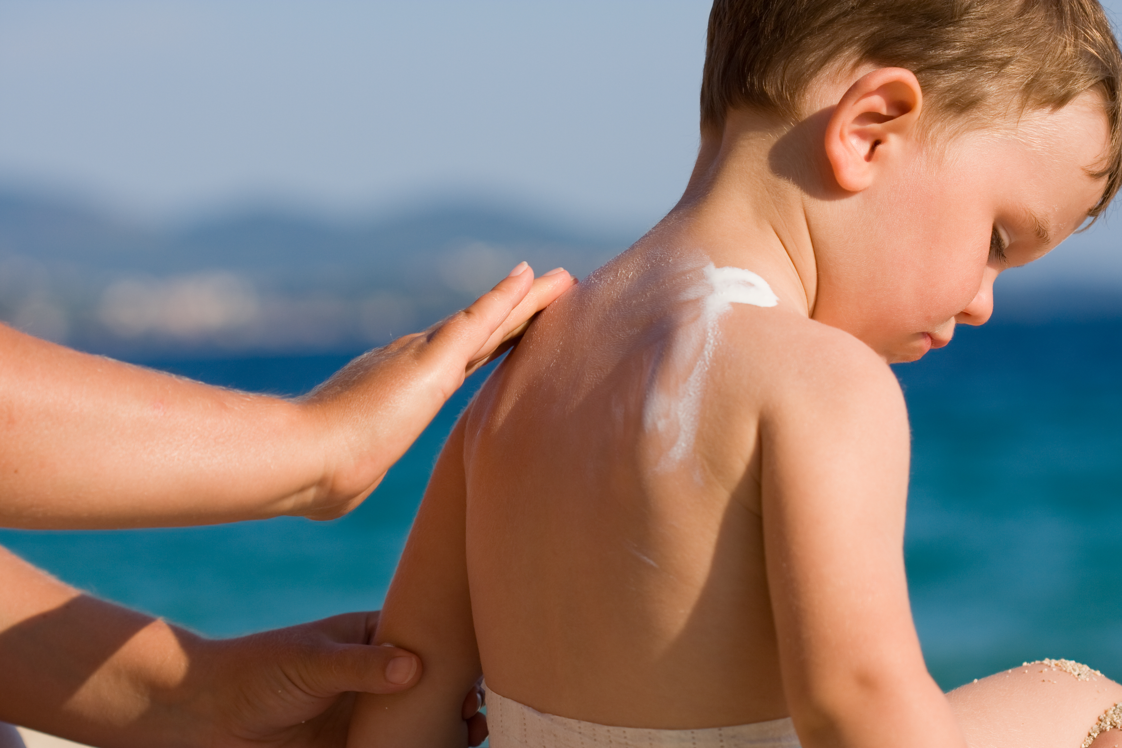 Förälder som smörjer barn med solskydd på stranden