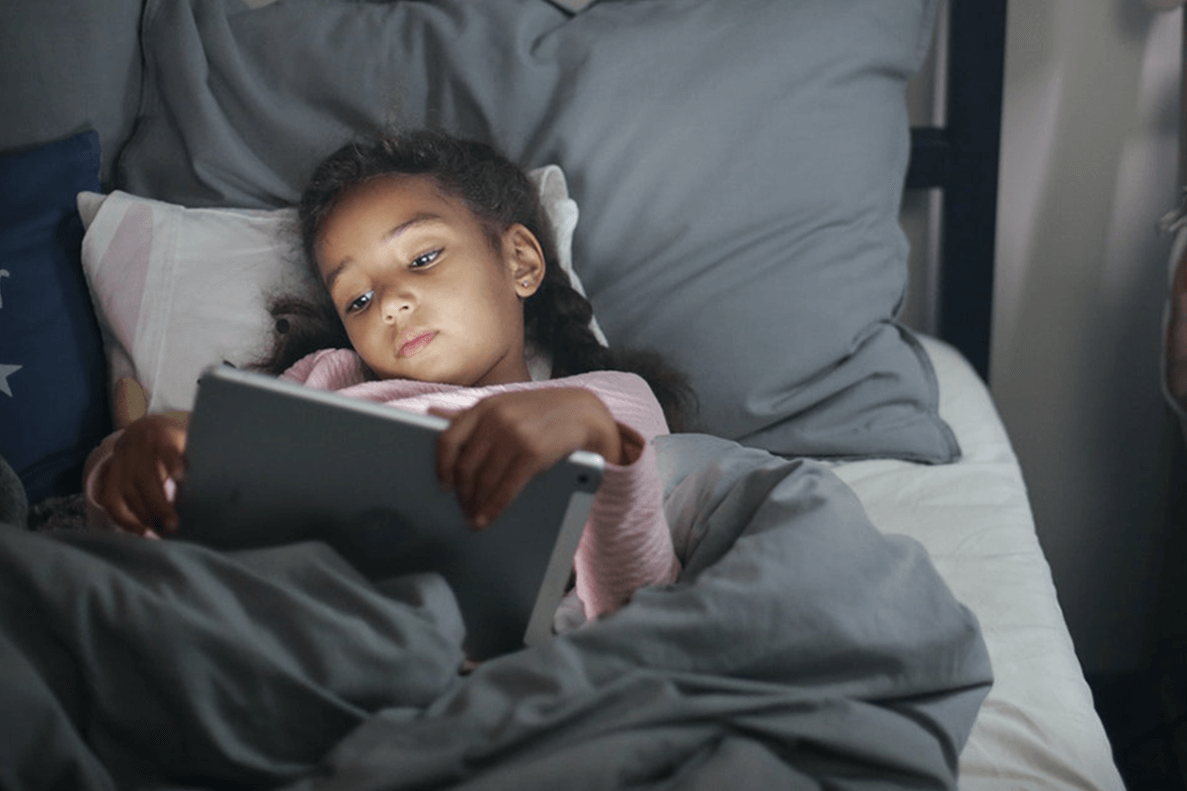 Flicka ligger i sin säng och tittar på iPad