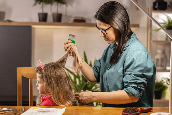 Mamma behandlar dotterns hår som är fullt med löss