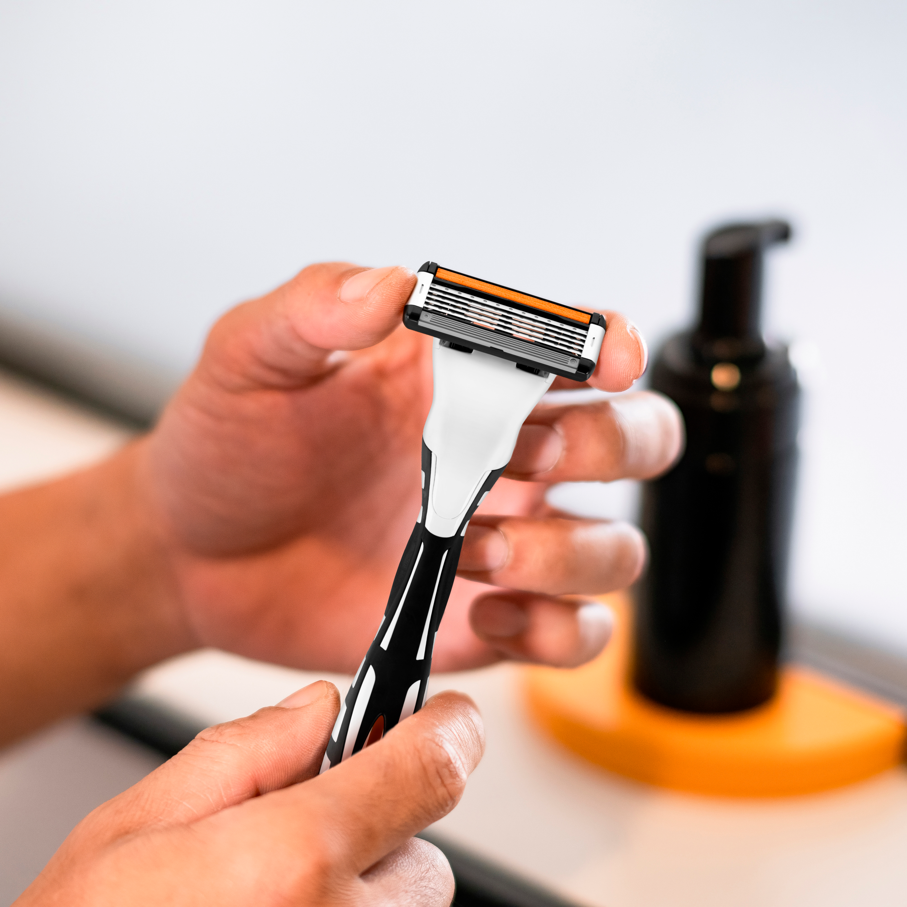 Händer håller en rakhyvel i badrumsmiljö.