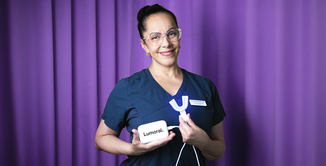 Tandvårdspersonal håller Lumoral-enhet mot lila bakgrund.